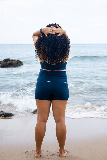 Красива фітнес-леді стоїть, роблячи верхнє тіло, що тягнеться на пляжі проти моря і хмарного неба. Здоровий спосіб життя. - Фото, зображення