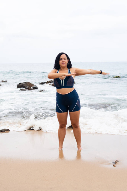 Kobieta fitness, stojąca, ćwicząca ramionami na plaży piasek o morze i zachmurzone niebo. Zdrowy styl życia. - Zdjęcie, obraz
