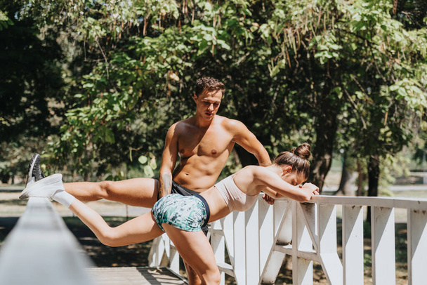 Couple caucasien faisant des exercices dans le parc, profiter de l'entraînement ensoleillé de l'été sur un pont. Motivés par la forme physique, ils s'entraînent en plein air avec des amis, des professionnels, dans un environnement naturel. - Photo, image