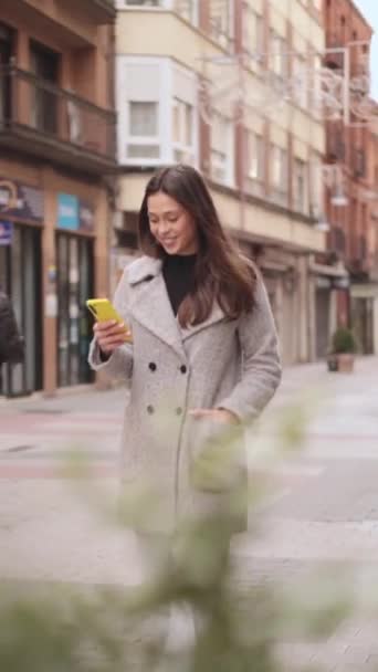 Молодая красивая женщина ходит по улице и пользуется мобильным телефоном. Бразильская этническая принадлежность. Высококачественные кадры - Кадры, видео