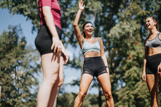 Спортивные женщины занимаются спортом на свежем воздухе в солнечном парке, прыгают и растягивают свои тела. Их энергия и счастье мотивируют друг друга в фитнес-путешествии.. - Фото, изображение