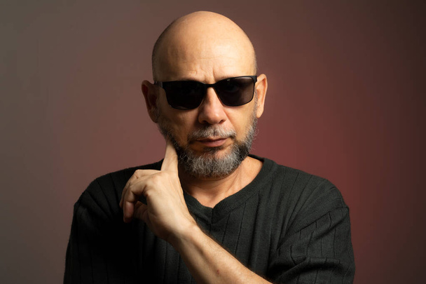 White, bald man, wearing sunglasses, confident and serious looking towards the camera. Isolated on red background. - Photo, Image