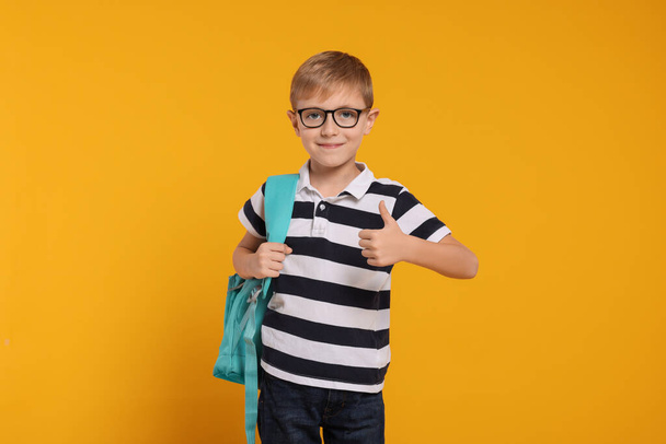 Happy schoolboy in glasses with backpack on orange background - Foto, afbeelding
