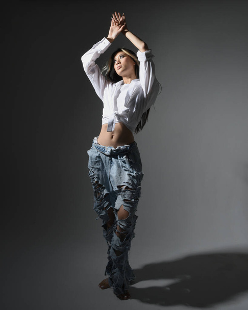 Портрет брюнетки жіночої азіатської моделі в повсякденному одязі, біла сорочка-синглет, джинсові штани. Позиція, що стоїть перед камерою. Ізольовані на білому фоні студії. - Фото, зображення