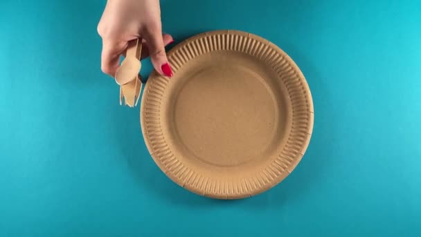 Eco-conscious lifestyle concept. Unrecognizable female hands carefully arrange eco-friendly disposable paper tableware on blue background, emphasizing environmental care and sustainability indoors - Footage, Video