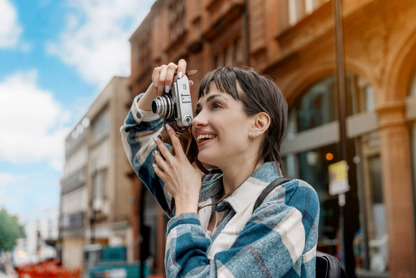 жінка в блакитній сорочці і кепці з рюкзаком, що йде містом, фотографує селфі, розважається як туристична концепція стилю життя - Фото, зображення