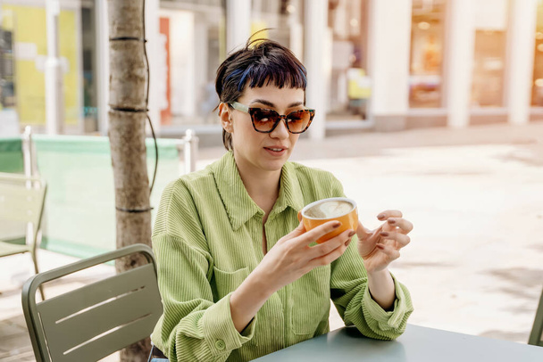 Женщина пьет кофе в уличном кафе, разговаривает по телефону и веселится. стиль жизни - Фото, изображение