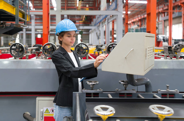 Μια γυναίκα χειρίζεται βιομηχανικό εξοπλισμό μέσα σε ένα πολυάσχολο εργοστασιακό περιβάλλον, διαχειριζόμενη επιδέξια τα μηχανήματα. - Φωτογραφία, εικόνα