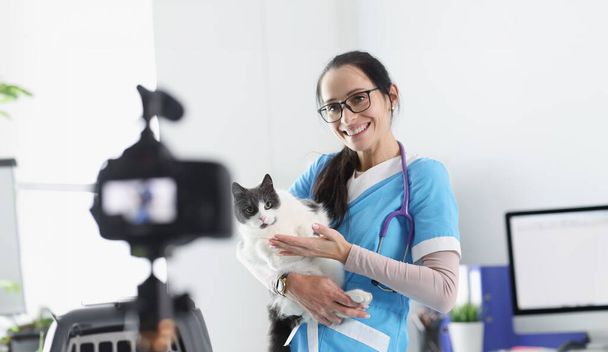 Usmívající se veterinární lékař demonstruje kočka do kamery. Péče o zvířata a léčba blog koncept - Fotografie, Obrázek