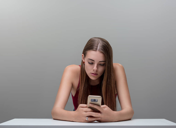Переповнений її телефоном, фокус жінки відображає поглинання цифрового віку, а верхня частина дичини контрастує з сірою - Фото, зображення