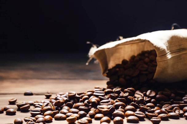 Los granos de café tostados frescos caen de una bolsa sobre una superficie de madera. Los granos de café marrón se dispersan de una bolsa en la mesa. Café. - Foto, Imagen