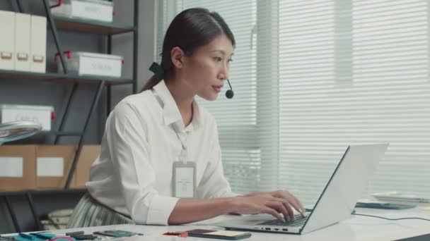Plan moyen de femme gestionnaire de centre de réparation consultation clients parlant dans casque assis en face de l'ordinateur portable - Séquence, vidéo