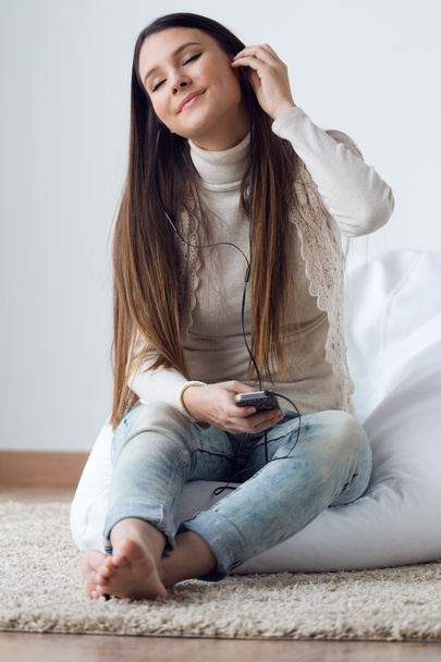 Молодая женщина слушает музыку мобильным телефоном у себя дома
 - Фото, изображение