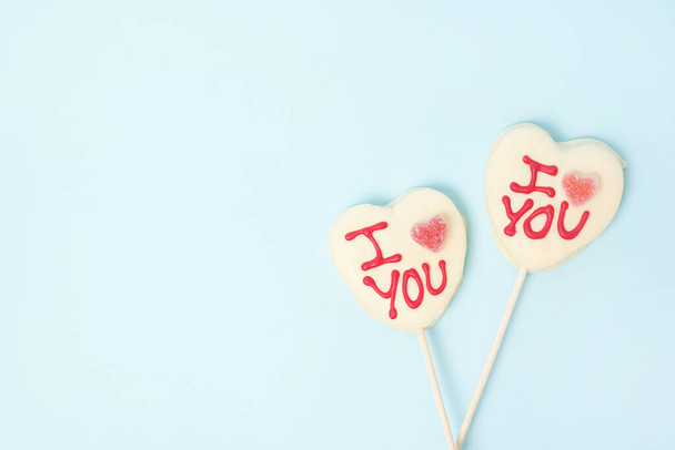 dos caramelos en forma de corazón del día de San Valentín con chocolate blanco sobre fondo de papel azul pastel. Concepto de amor - Foto, Imagen