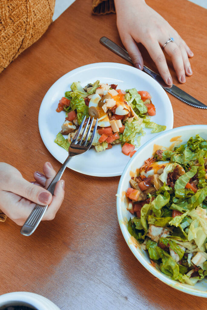 vertical image of unrecognizable woman sitting eating salad with fork in restaurant, copy space - Photo, Image
