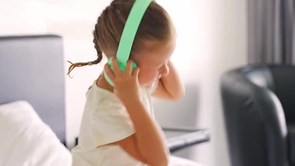 Χαμογελαστό κοριτσάκι συναισθηματικό απολαμβάνοντας μουσική χρησιμοποιώντας πράσινα παιδικά ακουστικά. Υψηλής ποιότητας 4k πλάνα - Πλάνα, βίντεο