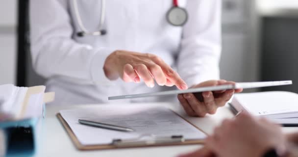 Arzt arbeitet mit Tablette bei Verabredung mit Patient. Gp-Arzt in weißer Uniform diskutiert die Ergebnisse der Patientendiagnose während er den Kunden auf dem Tablet-Bildschirm berät. - Filmmaterial, Video