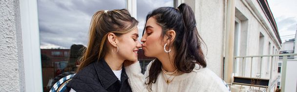 молодая лесбиянка целует нос своей девушки, сидя вместе на балконе, плакат - Фото, изображение