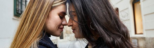 vista lateral de feliz pareja lesbiana en ropa de abrigo de pie cara a cara al aire libre, pancarta horizontal - Foto, imagen