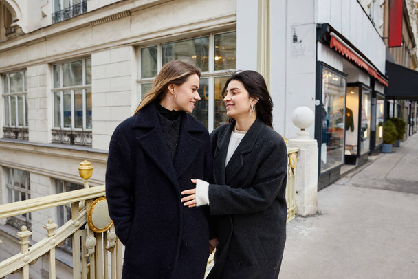Intiem moment van vrolijke lesbische vrouwen in liefde staan samen op straat in de Europese stad - Foto, afbeelding