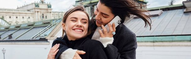 boldog leszbikus nő beszél okostelefonon, és megöleli a barátnőjét utazás közben Bécsbe, banner - Fotó, kép