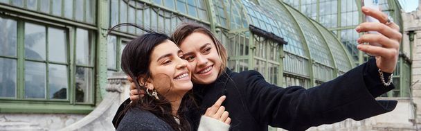 szczęśliwa lesbijka para biorąc selfie stojąc w pobliżu historycznego miejsca w Wiedniu, poziomy baner - Zdjęcie, obraz