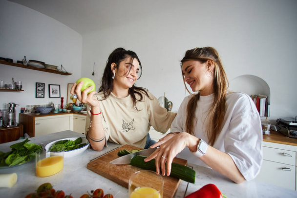 счастливая молодая лесбийская пара улыбается во время приготовления салата вместе на современной кухне, lgbtq концепция - Фото, изображение
