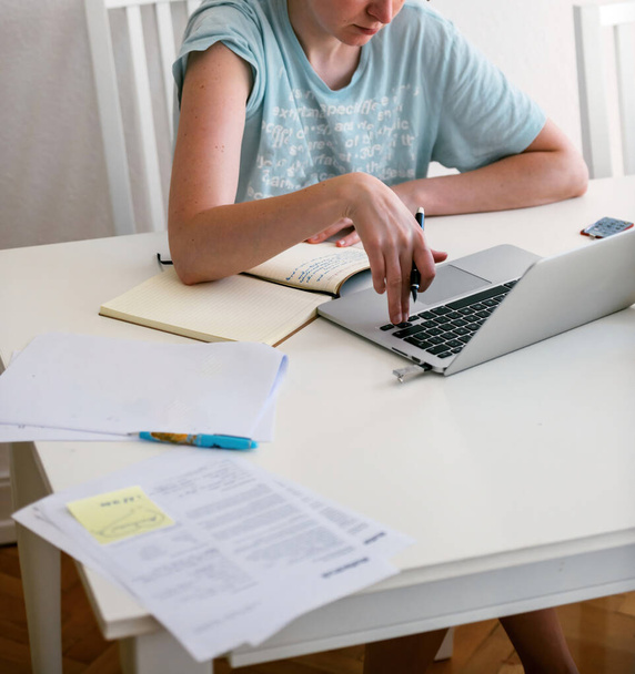 Una donna, serena e concentrata, digita su un computer portatile argentato, circondata da appunti, lavorando diligentemente al suo significativo progetto di dottorato - Foto, immagini