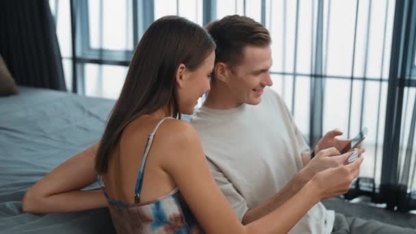 若いカップルは,クレジットカードで支払うためにスマートフォンでオンライン決済アプリとデジタルウォレットを使用してホームベッドルームに座っています. モバイルインターネットを介して商業ショッピングとモダンな購入. アディット - 映像、動画