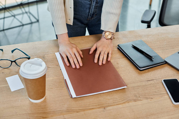 Μια σύγχρονη επιχειρηματίας κάθεται σε ένα τραπέζι με τα χέρια της σε ένα ανοιχτό βιβλίο, πλήρως αφοσιωμένη στην επέκταση των γνώσεών της. - Φωτογραφία, εικόνα