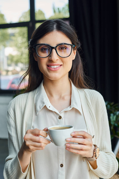 Gözlüklü bir iş kadını modern bir ofis çalışma alanında kahve molası verir.. - Fotoğraf, Görsel