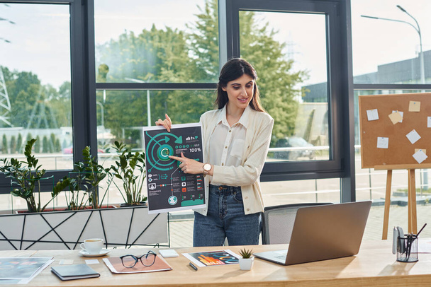 Una mujer de negocios se encuentra confiada en una oficina moderna, sosteniendo un cartel para transmitir su mensaje en un entorno de concepto de franquicia. - Foto, imagen