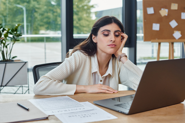Деловая женщина сидит за столом в современном офисе, сосредоточенном на ноутбуке, воплощая концепцию процветающей франшизы. - Фото, изображение