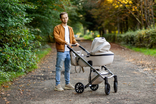 Padre con hijo pequeño caminando en cochecito de bebé en el parque otoñal. Pasar tiempo con el recién nacido y respirar aire fresco. - Foto, imagen