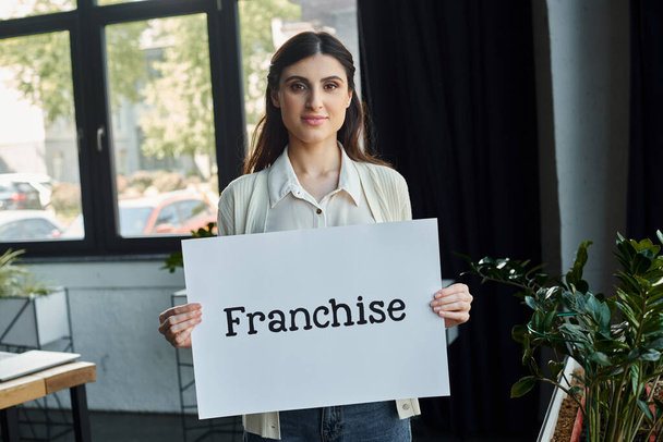 Nowoczesna bizneswoman biurowa pewnie trzyma napis "franczyza" w symbolicznym geście przedsiębiorczości.. - Zdjęcie, obraz