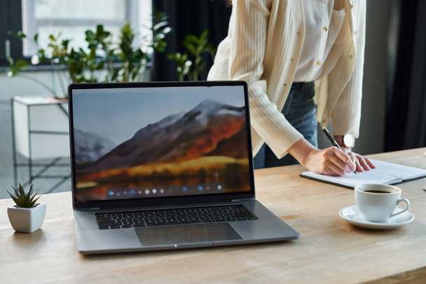Une femme d'affaires concentrée utilisant un ordinateur portable sur une table en bois dans un cadre de bureau moderne, incarnant le concept de franchise. - Photo, image