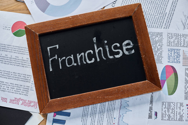 Доска со словом "франшиза", написанная смелым мелом, символизирующая расширение бизнеса и рост в современной офисной обстановке. - Фото, изображение