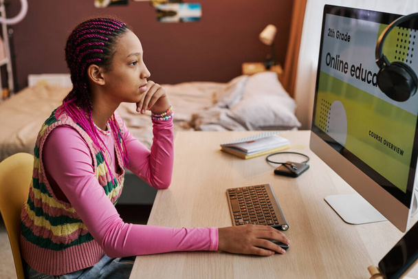 Side view muotokuva musta teini tyttö käyttää tietokonetta kotona ja selailu verkossa koulutus verkkosivuilla - Valokuva, kuva
