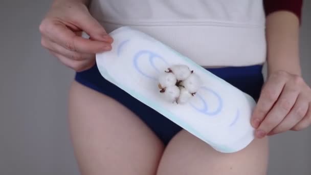 サニタリーナプキンと綿花. 女の子は彼女のパンティの背景に対して綿の衛生パッドを示しています. 女性月経のためのプラスチックフリー製品の概念. エコフレンドリーな製品 - 映像、動画