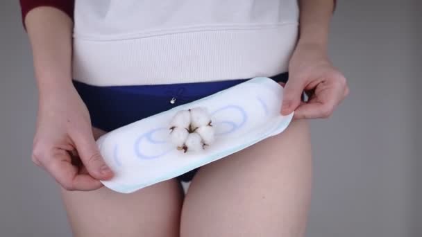 サニタリーナプキンと綿花. 女の子は彼女のパンティの背景に対して綿の衛生パッドを示しています. 女性月経のためのプラスチックフリー製品の概念. エコフレンドリーな製品 - 映像、動画