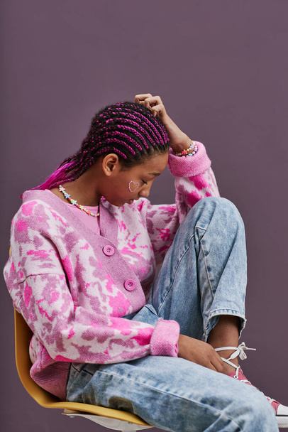Vertikální boční pohled portrét černošky dospívající dívka na sobě trendy ležérní oblečení pózování sedí na židli s nohama nahoru - Fotografie, Obrázek