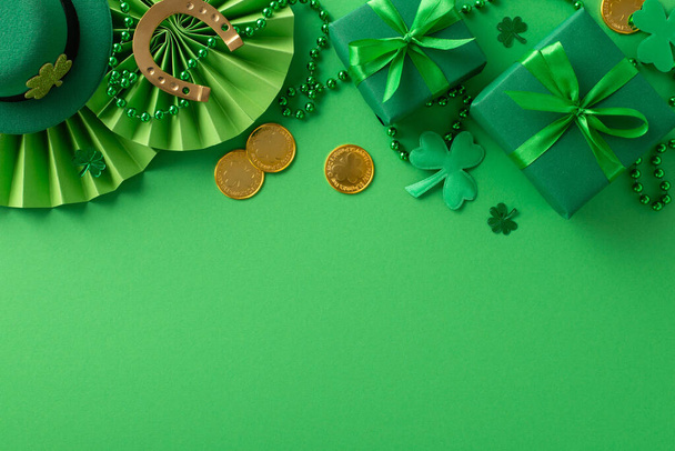 Festive St. Paddy's setup: Overhead shot featuring Irish charm. Leprechaun's hat, gift boxes, horseshoe, gold coins, fans, shamrocks, beads on green backdrop. Ad space available - Photo, Image