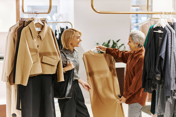 Boční pohled portrét prodejce asistent pomáhá starší ženy výběru oblečení v luxusním butiku - Fotografie, Obrázek