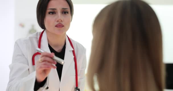 Konzentrierte Therapeutin beleuchtet Patientin mit Taschenlampe zur eingehenden Untersuchung im Krankenhaus. Beruflicher Termin und Beschwerden von Frauen über sich verschlechternde Gesundheit - Filmmaterial, Video