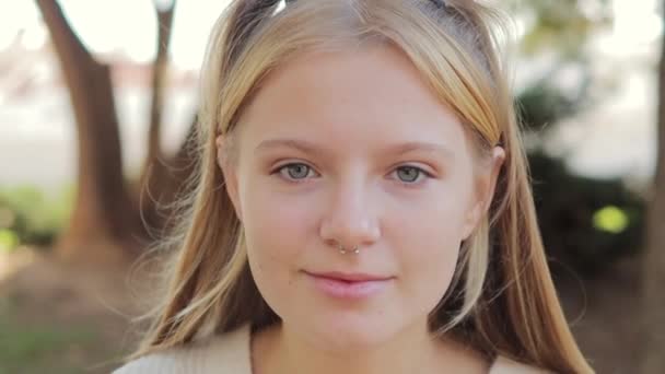 Happy young hipster generation Z teenage girl smiling face with blonde hair and nose piercing looking at camera while posing outdoors in park Headshot close up portrait. High quality FullHD footage - Footage, Video