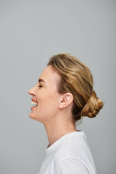 iloinen houkutteleva nainen kerätty vaaleat hiukset poseeraa harmaa tausta ja nauraa vilpittömästi - Valokuva, kuva