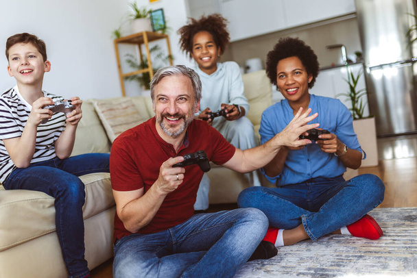 Lachende familie genieten van tijd samen thuis zitten op de bank in de woonkamer en videospelletjes spelen. - Foto, afbeelding