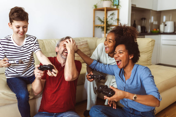 Усміхнена сім'я насолоджується разом вдома сидячи на дивані у вітальні та граючи у відеоігри
. - Фото, зображення