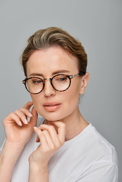 good looking blonde woman with collected hair and glasses posing on gray backdrop and looking away - Photo, Image
