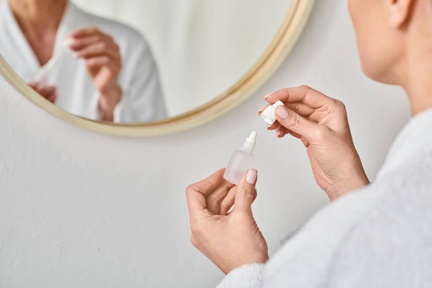 обрезанный вид взрослой женщины в халате с помощью глазных капель перед зеркалом в ванной комнате - Фото, изображение
